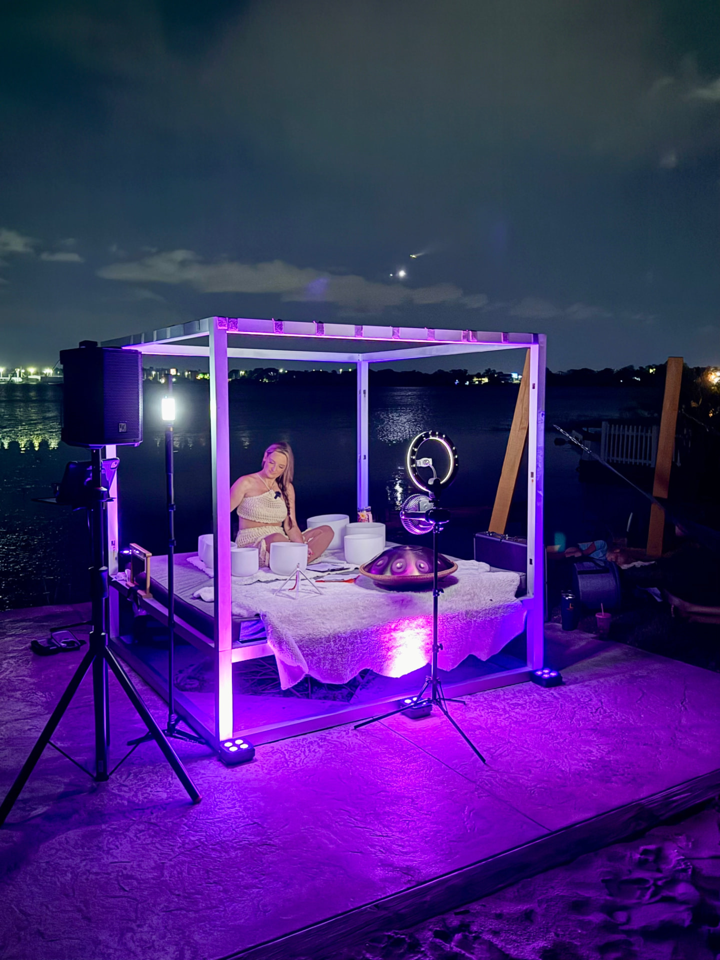 Waterfront evening sound bath under violet lights with crystal bowls and handpan