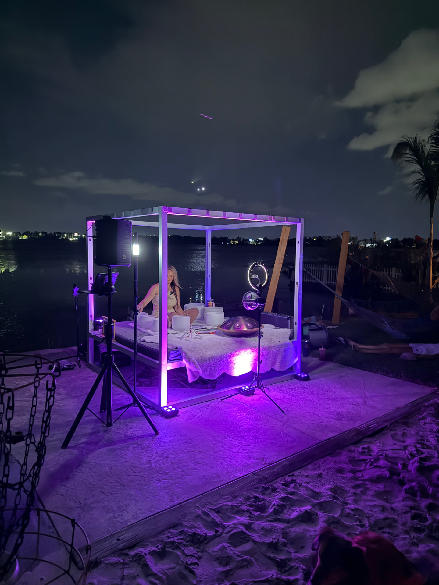 Nighttime waterfront sound bath in a violet-lit cube with crystal bowls and handpan